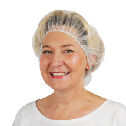 A smiling blonde woman wears the ARNOMED COVER PP-BARETTHAUBE made of PP non-woven fabric by ARNOWA GmbH and a white shirt and poses in front of a plain white background - ideal for the hygiene sector.