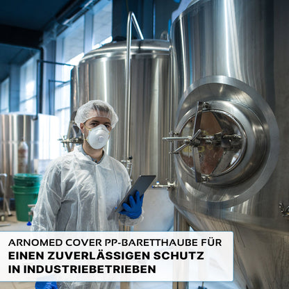 A person in protective clothing, including the ARNOMED COVER PP-BARETTHAUBE by ARNOWA GmbH and a mask, holds a tablet next to stainless steel tanks in a hygienic industrial area. The German text about reliable protection is displayed below.