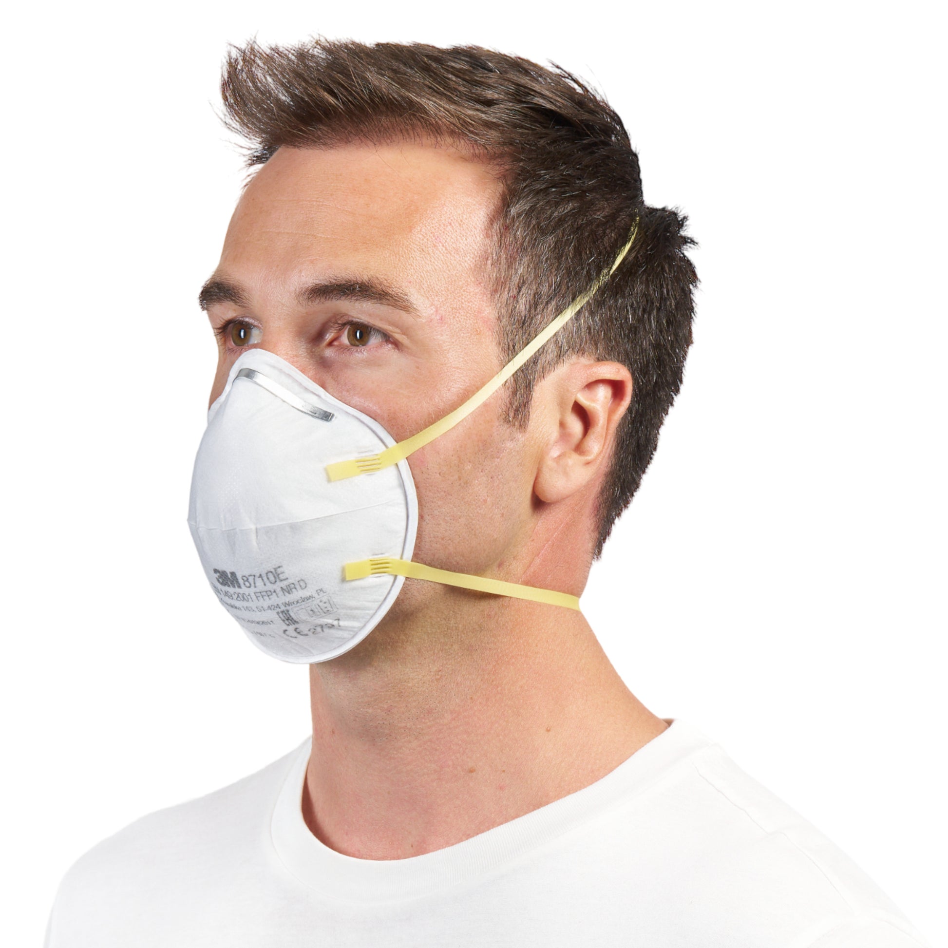 Ein Mann mit kurzen braunen Haaren trägt eine 3M™ Partikelmaske 8710E FFP1 (von 3M Deutschland GmbH) mit gelben Bändern und ohne Ventil über Nase und Mund, gepaart mit einem schlichten weißen Hemd vor einem weißen Hintergrund.
