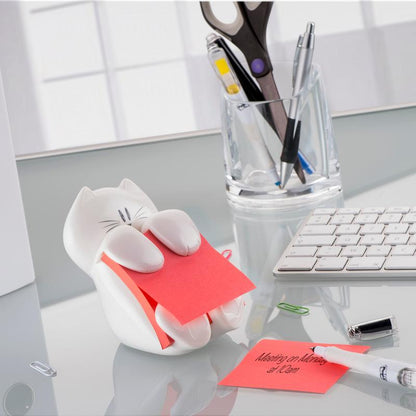 On a glass table stands the 3M Post-it® Z-Notes Dispenser, Cat, White with a pink Post-it® Super Sticky Z-Note (76x76mm) from 3M Deutschland GmbH. Nearby are a keyboard, pens in a glass cup, scissors, paper clips, and a handwritten note.