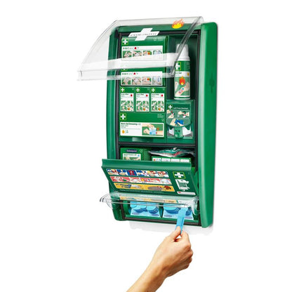 A wall-mounted Cederroth first aid & burn station from Orkla Wound Care AB is open, showing supplies like bandages, instructions, eye wash bottles, and a hand taking a blue eye wash capsule from the lower compartment. (1 package/carton).