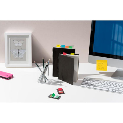 On the desk are 3M Post-it® Index Tabs, notebooks with colorful tabs, a pen cup, an eraser, a stapler, a framed butterfly print, and a computer screen with a yellow sticky note.