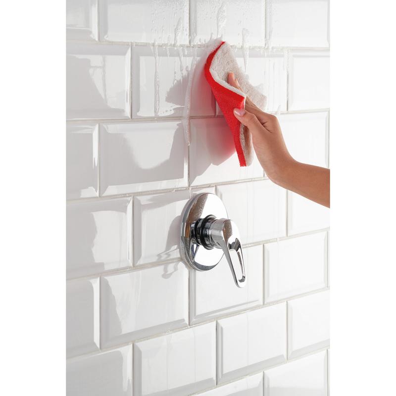 With the Scotch-Brite® Bath XXL cleaning sponge from 3M Deutschland GmbH, a hand removes limescale deposits from white tiles in the shower, while water drips and a silver shower handle is visible.