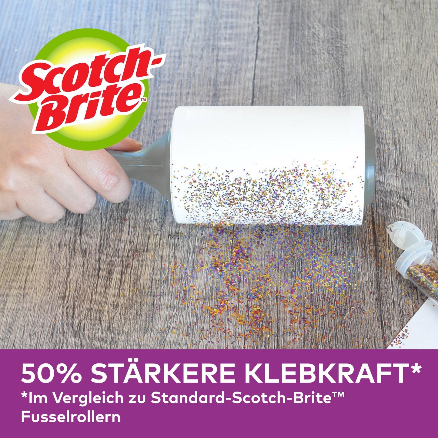 Eine Hand benutzt die Scotch-Brite™ Pet Extra Sticky* Ersatzrolle für Tierhaare (48 Blatt, 1/Packung) von 3M Deutschland GmbH, um verschütteten Glitter von Holz zu entfernen. Ein offener Glitterbehälter ist in der Nähe. "50% stärkere Klebekraft" im Vergleich zu den unten abgebildeten Standardrollen.