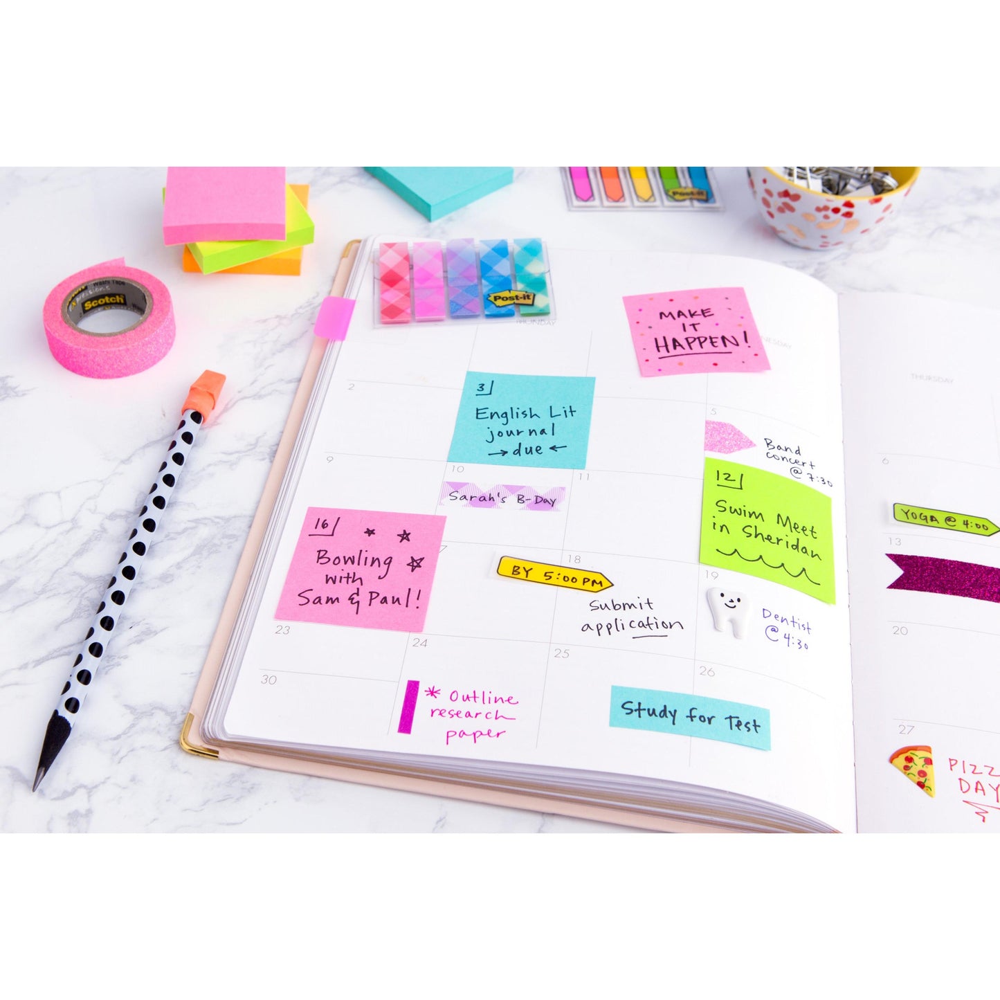 On a white desk lies an open planner with handwritten notes, a striped pen, office supplies, and colorful Post-it® notes (76 mm x 127 mm, 100 sheets/block, 100% PEFC) from 3M Deutschland GmbH for marking tasks and appointments.