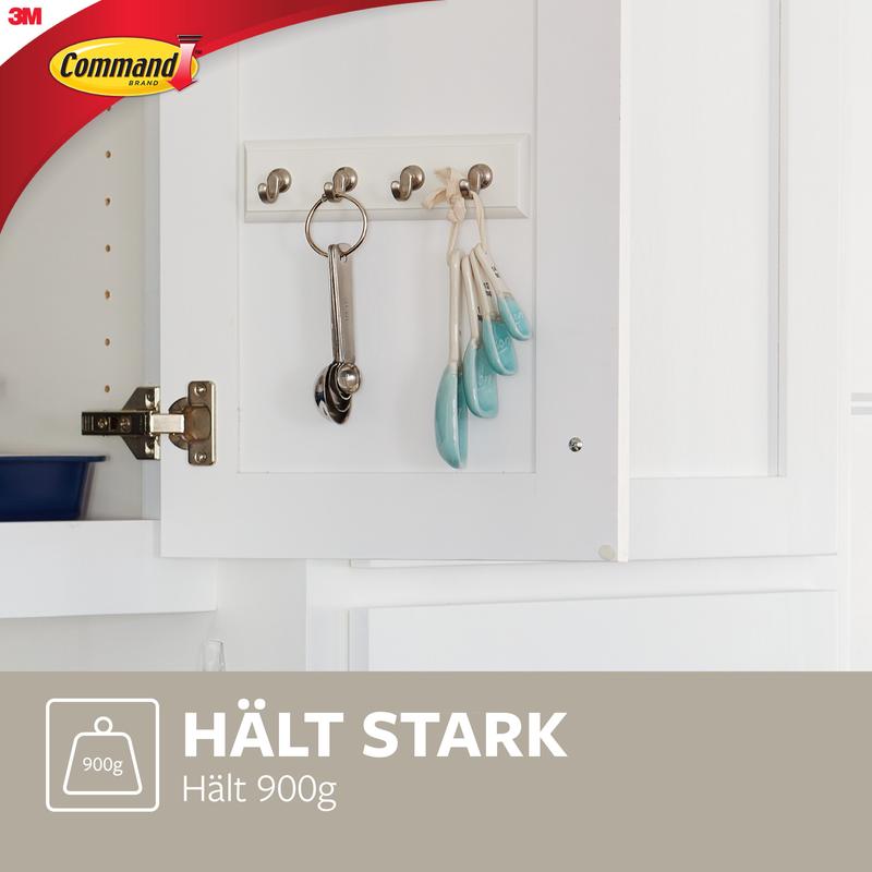 A white Command™ key rail in quartz (HOM18-Q) from 3M Deutschland GmbH with metal hooks holds keys, measuring spoons, and a key ring. Below it says "HOLDS STRONGLY Holds 900g" with a weight symbol and 3M Command logo.