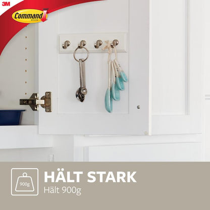 A white Command™ key rail in quartz (HOM18-Q) from 3M Deutschland GmbH with metal hooks holds keys, measuring spoons, and a key ring. Below it says "HOLDS STRONGLY Holds 900g" with a weight symbol and 3M Command logo.