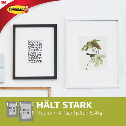 Two framed pictures hang on a white wall; one with black-and-white faces, the other a botanical illustration. Medium Command™ Picture Hanging Strips M 17201-4PK from 3M Deutschland GmbH offer strong adhesive power without wall damage.