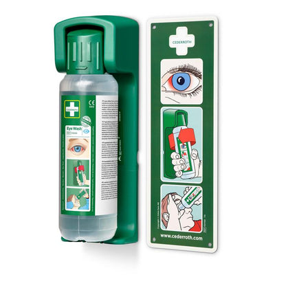 Pictured is a wall-mounted Orkla Wound Care AB holder for 500 ml eye wash with a glow-in-the-dark instruction sign and a clear instructional diagram for step-by-step eye wash guidance.