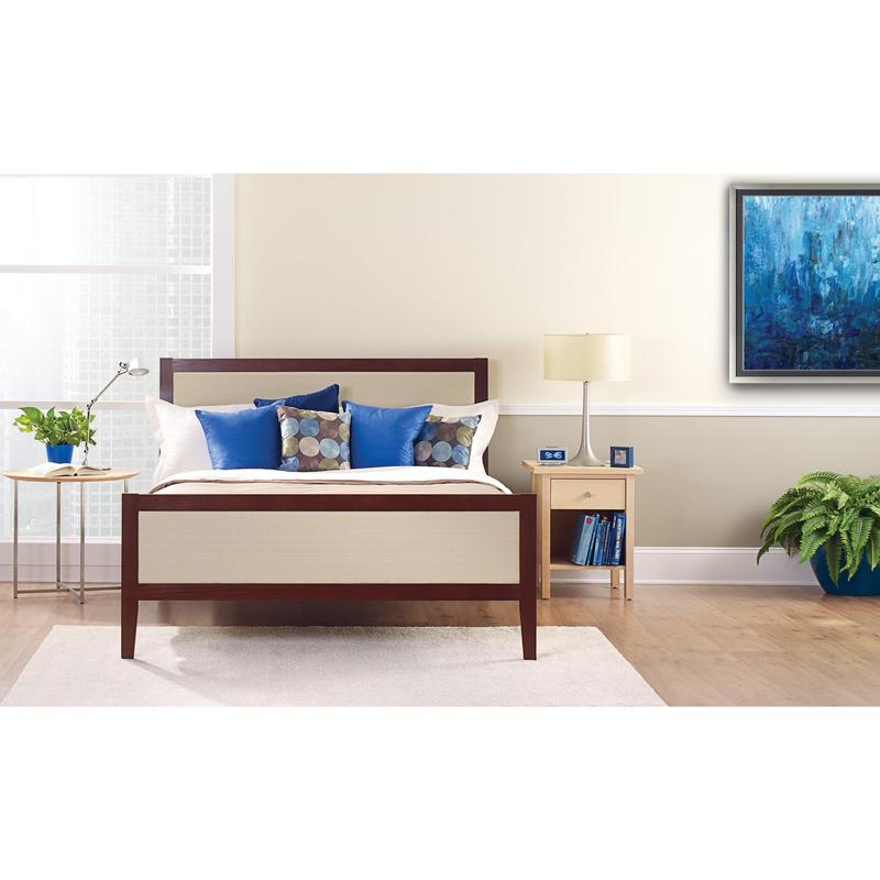 A neatly made bed with white and blue pillows stands in front of a light wall that is taped with ScotchBlue™ Painter's Tape "Multi-Surface" by 3M Deutschland GmbH. On a bedside table are a lamp, a clock, books, and a potted plant next to the bright window.