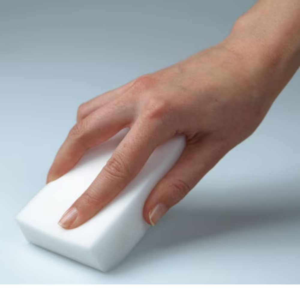 A hand holds a Vileda Professional Miraclean Dirt Eraser Big, a white, rectangular sponge measuring 12x7.5x2.8 cm, and presses it against a smooth, light surface to effortlessly remove even the most stubborn stains.