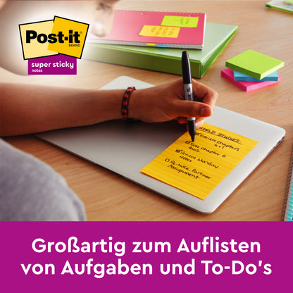 Eine Person notiert Aufgaben auf grünen, linierten Post-it® Super Sticky Notes im Großformat (101 x 101 mm) von 3M Deutschland GmbH, die auf einem Laptop liegen. Notizbücher, ein Stift und andere bunte Notizzettel im Großformat liegen in der Nähe verstreut. Der deutsche Text wirbt für die Verwendung von Post-its.