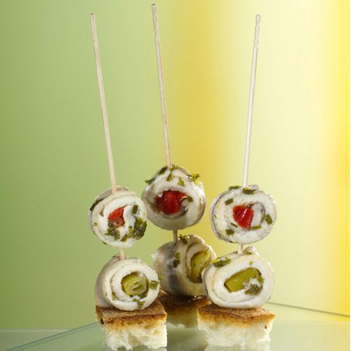 Four skewers with rolled white meat, filled with green herbs and red pepper, are served on bread and presented with the PAPSTAR Fingerfood-Picker "pure" 15 cm from PAPSTAR GmbH against a green-yellow gradient.