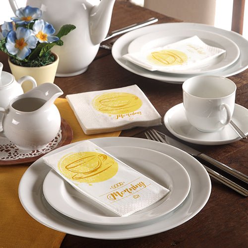 A neatly set table with white tableware, a teapot, blue flowers, and 3-ply PAPSTAR-Napkins (33 x 33 cm) from the PAPSTAR GmbH with a yellow coffee mug and the word "Morning."