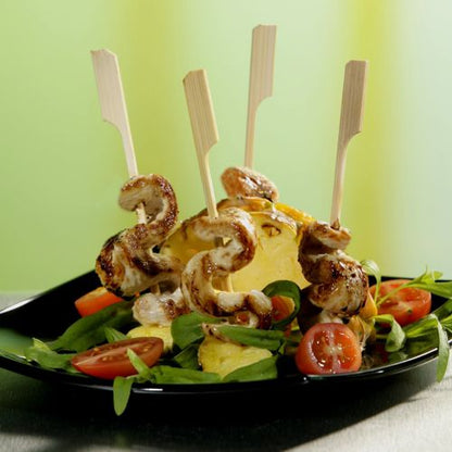 PAPSTAR 21 cm "Golf" grill skewers from PAPSTAR GmbH: Perfect BBQ and grill party skewers made of chicken and pineapple on fresh salads with cherry tomatoes, served on a black plate against a green-yellow background. 250 pieces in a cardboard tray.