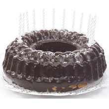 A chocolate cake with shiny glaze, decorated with PAPSTAR GmbH birthday candles 6 cm, white with holder (24 pieces), which are evenly distributed around the edge and lie on a white lace doily.