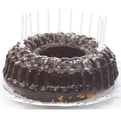 A chocolate cake with shiny glaze, decorated with PAPSTAR GmbH birthday candles 6 cm, white with holder (24 pieces), which are evenly distributed around the edge and lie on a white lace doily.