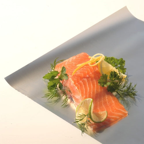 Two raw salmon fillets lie on a sheet of Starpak loose aluminum foil by Starpak, garnished with lemon and lime slices as well as fresh parsley and dill. The background is plain and brightly lit.