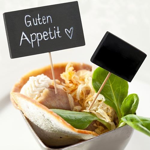 A small bowl with leafy greens, crispy fried onions, bread, and white spread contains two PAPSTAR 100 Fingerfood - Picker Sticks from PAPSTAR GmbH - one says "Guten Appetit ♥" and the other has a writable board.