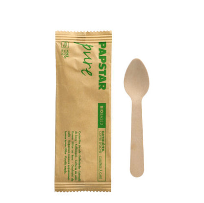 An eco-friendly PAPSTAR wooden coffee spoon, 11 cm, individually wrapped in shrink wrap, lies next to its "pure" packaging with green lettering of the brand PAPSTAR GmbH on a plain white background.