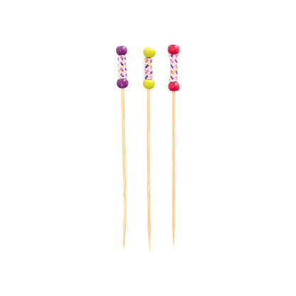 Three PAPSTAR 100 finger food picks from PAPSTAR GmbH made of bamboo stand upright. Each pick has a decorative handle with colorful beads (purple, yellow, pink) and a cross pattern.