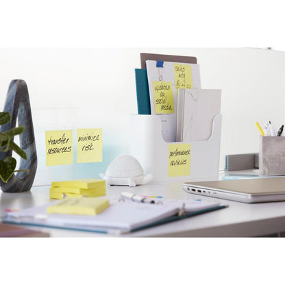 A tidy office desk with folders, 3M Post-it® Super Sticky Z-Notes, Yellow (76 mm x 76 mm), a turtle figurine, a plant, pens, a closed laptop, and papers. The notes on the folders read "Performance Review" and "Minimize Risk."