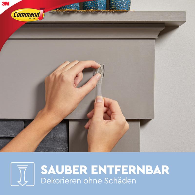 A person pulls a transparent adhesive strip from a gray mantel and shows how Command™ Mini Hooks, transparent, with transparent strips (17006CLR) from 3M Deutschland GmbH can decorate and attach without a trace. Command and 3M logos are visible.