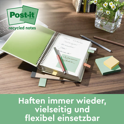 A desk with an open notebook with Post-it® Super Sticky 100% Recycled Notes (47.6 mm x 47.6 mm, 70 sheets/block, 100% PEFC) from 3M Deutschland GmbH, a ballpoint pen and pencil, paper clips, and a glass vase with green leaves. The German text appears below.