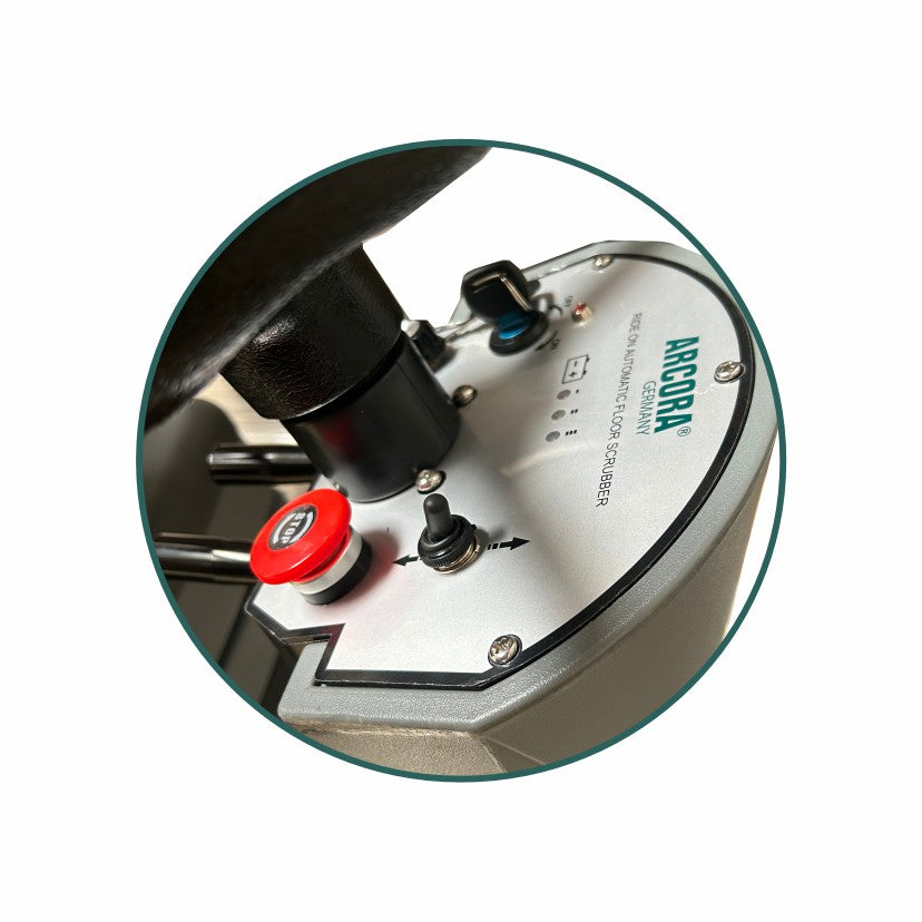 Nahaufnahme des Bedienfelds der Arcora Ro-Man 660Br/90L Aufsitz-Scheuersaugmaschine der Arcora International GmbH mit Schaltern, Kontrollleuchten und einer Not-Aus-Taste auf einer Metalloberfläche.