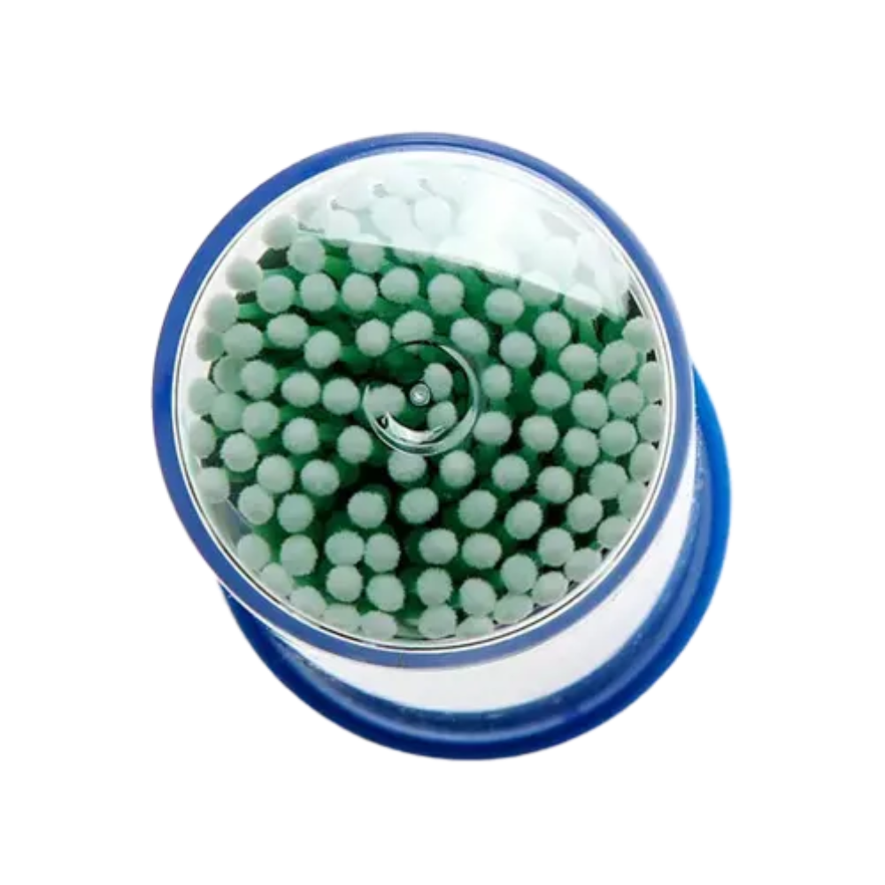 Viewed from above, a cylindrical container with a blue base and transparent lid is shown, containing white AMPri MED-COMFORT disposable micro applicators with green tips. These are commonly used in dental supplies for precise work in cosmetic or medical applications.