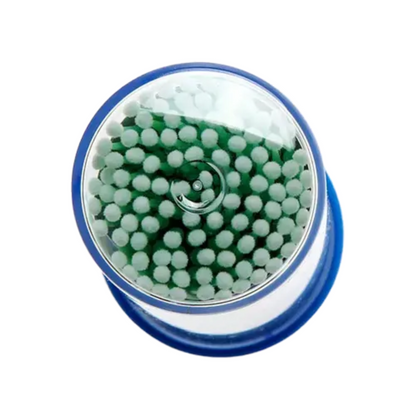 Viewed from above, a cylindrical container with a blue base and transparent lid is shown, containing white AMPri MED-COMFORT disposable micro applicators with green tips. These are commonly used in dental supplies for precise work in cosmetic or medical applications.