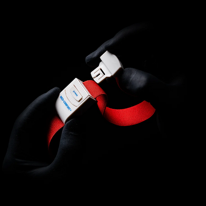 Gloved hands, reminiscent of an AMPri MED-COMFORT tourniquet, grip the buckle of a bright red safety belt against a shaded background. The word "Blue" and the letter "B" can be seen on the buckle.