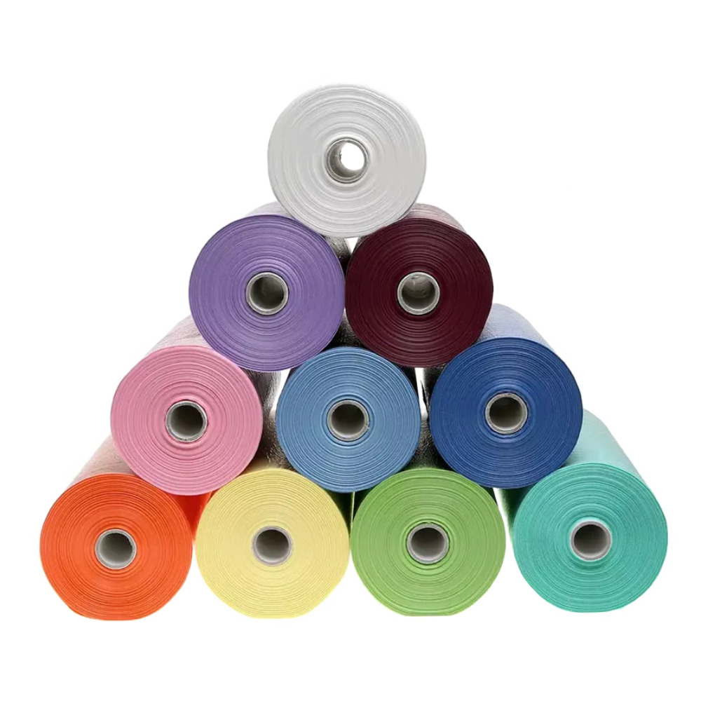 A pyramid-shaped stack of ten bright AMPri patient gown rolls in colors like white, purple, burgundy, pink, blue, teal, orange, yellow, green, and silver with PE coating from AMPri Handelsgesellschaft mbH glitters against a white background.