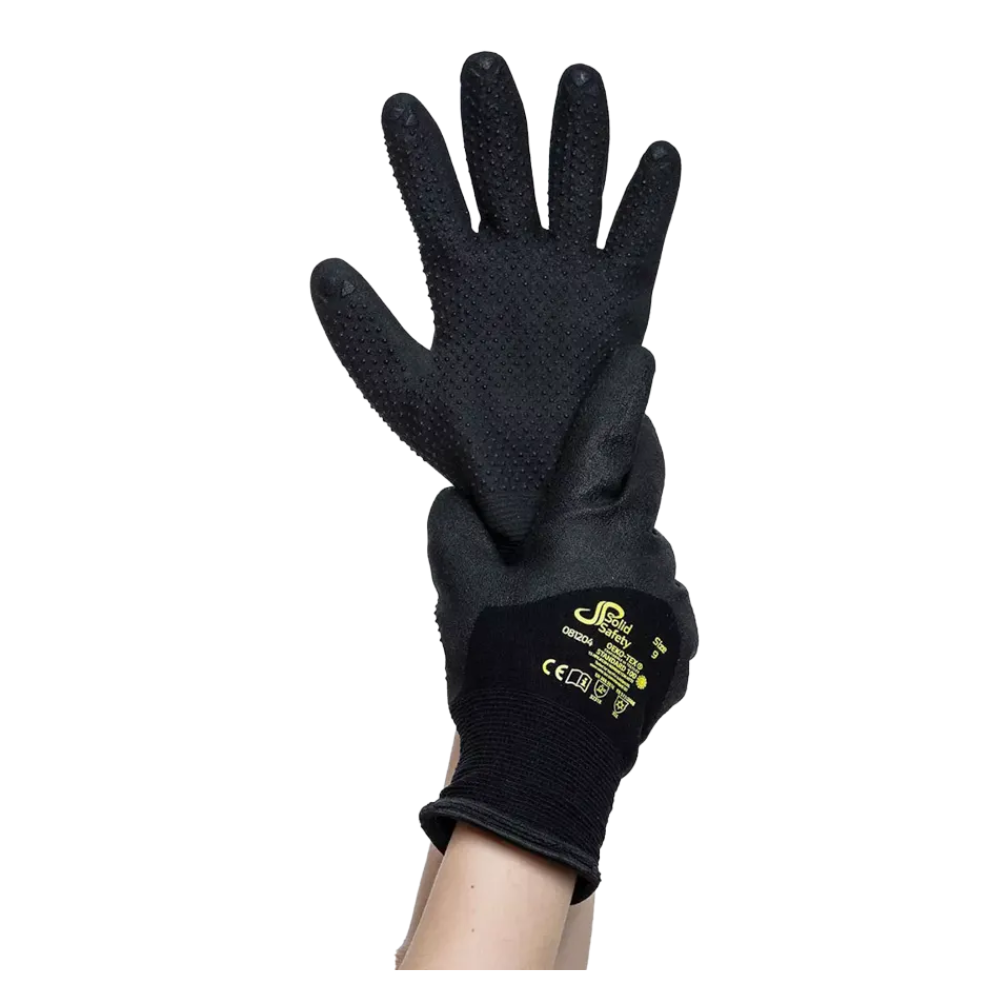 A pair of black AMPri SolidSafety Tough Winter Dots cold-resistant protective gloves with textured palms is held up by a hand. These gloves, designed to improve fine motor skills, feature the yellow trademark and safety certification marks of AMPri Handelsgesellschaft mbH on the back.