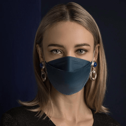 A person with long hair wears a blue Altruan designer face mask particle-filtering, providing effective protection according to FFP2 standard. She pairs it with large decorative earrings in front of a dark background and wears a black shirt.