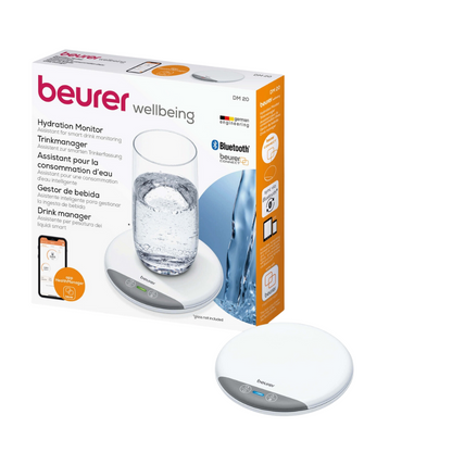 The image shows a Beurer DM 20 Drink Manager Hydration Monitor in its packaging. The box presents the product next to a glass of water and emphasizes its Bluetooth connectivity. The device is a small, white round pad with two touch-sensitive buttons and can be easily integrated with the beurer HealthManager Pro.