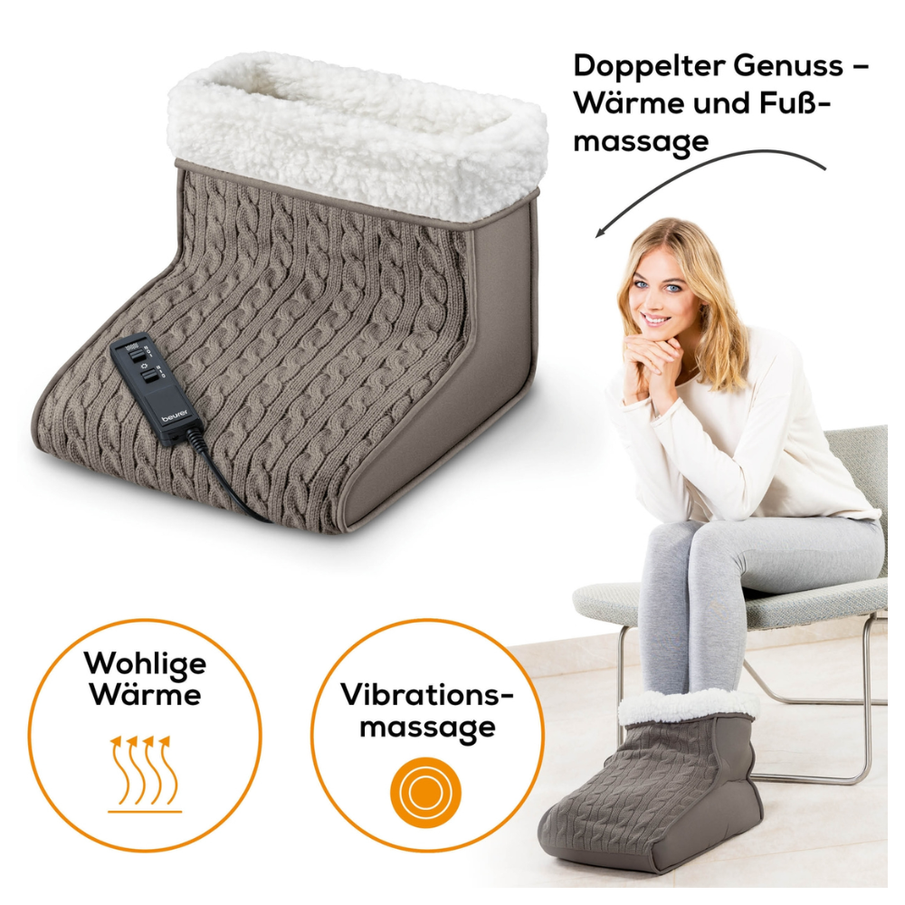A woman with large feet sits on a chair, her feet comfortably nestled in a gray cable-knit massage foot warmer Beurer FWM 45. The device from Beurer GmbH features multiple heat levels and comes with a remote control. The text in German reads: "Double Enjoyment – Heat and Foot Massage" and "Cozy Warmth" and "Vibration Massage."