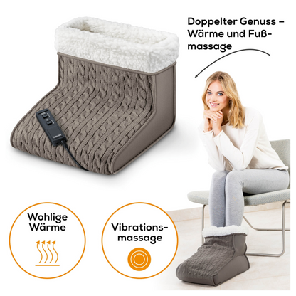 A woman with large feet sits on a chair, her feet comfortably nestled in a gray cable-knit massage foot warmer Beurer FWM 45. The device from Beurer GmbH features multiple heat levels and comes with a remote control. The text in German reads: "Double Enjoyment – Heat and Foot Massage" and "Cozy Warmth" and "Vibration Massage."