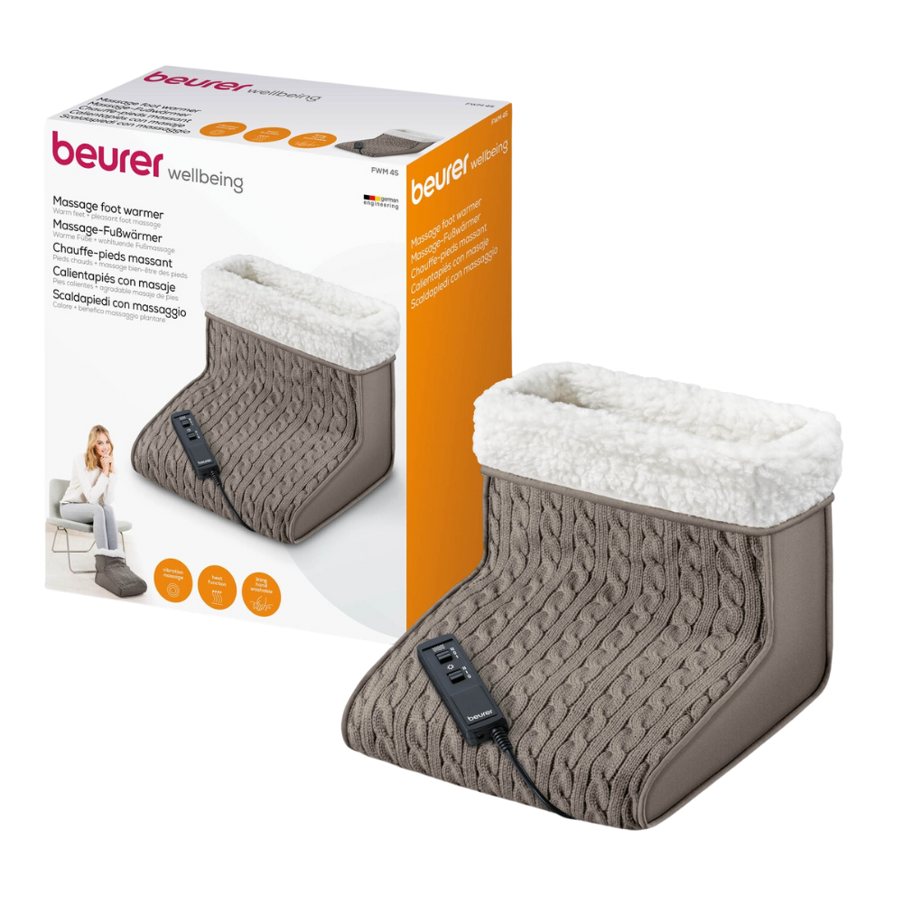 Displayed is a packaged Beurer FWM 45 massage foot warmer from Beurer GmbH. The white box shows a picture of the product and a woman using it. The foot warmer is made of gray knit with white plush lining and a black control unit for adjustable heat levels. The product name "Beurer FWM 45 Massage Foot Warmer | Package (1 piece)" is printed in several languages.