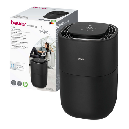 A black Beurer LB 200 humidifier from Beurer GmbH is placed next to its packaging box, which features, besides the brand name, a picture of the humidifier and a multilingual text stating that it is suitable for rooms up to 20 square meters. A woman is visible in the picture on the box.