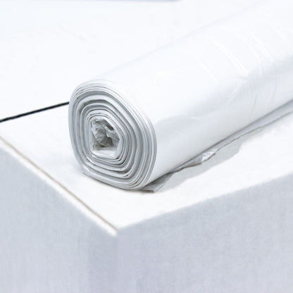 A roll of DEISS HDPE garbage bags 20 liters, 59906, white from EMIL DEISS KG (GmbH + Co.) lies on the edge of a white surface made from recycled material. The bags are neatly rolled and have multiple layers. The plain white background emphasizes the texture and high film elasticity of the plastic.