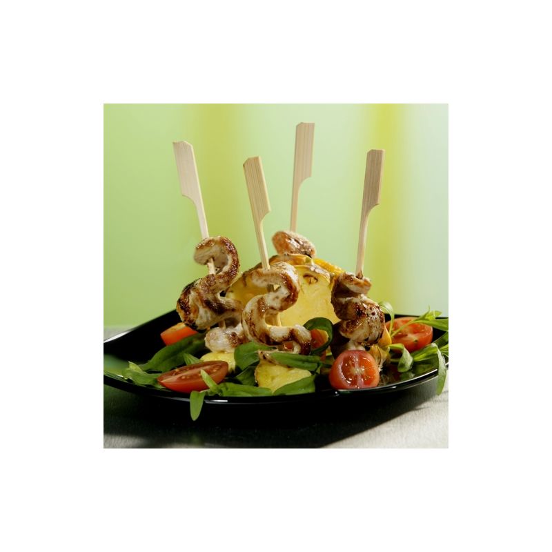 A black plate with a salad of leafy greens, cherry tomatoes, cucumbers, yellow cheese, and four shrimp, skewered on PAPSTAR 250 Fingerfood - Skewers "pure" from PAPSTAR GmbH, arranged vertically.
