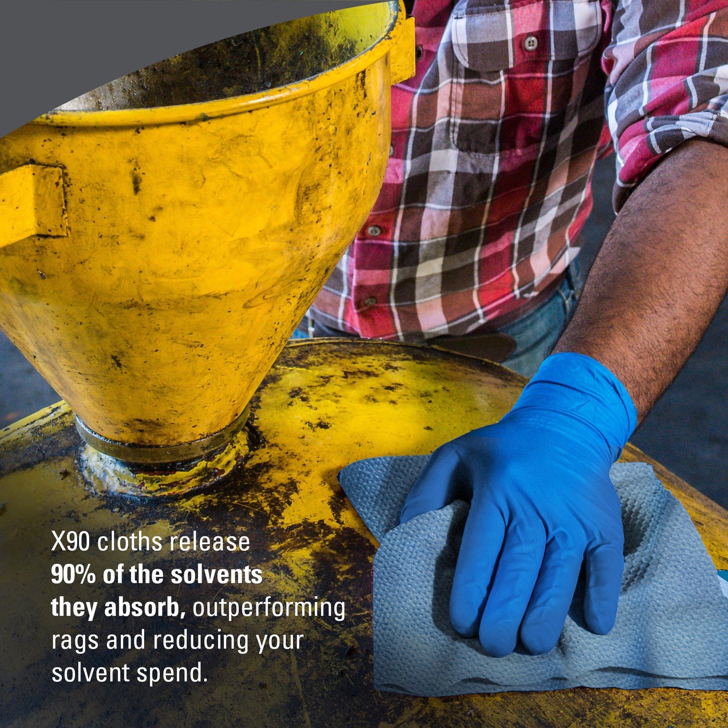 A person with a blue glove wipes a yellow industrial tank with a gray cloth. The text reads: "WypAll® X90 PowerClean from Kimberly-Clark absorbs and releases 90% of solvents, outperforming rags and reducing solvent costs.