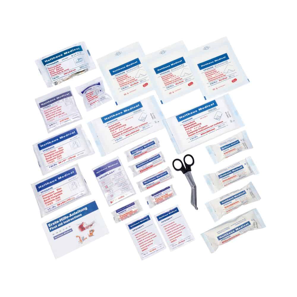 A Holthaus Medical complete assortment first aid kit DIN 13169 from Holthaus Medical GmbH & Co. KG with various medical items is spread out. The items include adhesive plasters, gauze compresses, antiseptic wipes, medical tape, and scissors. Each item of this filled first aid kit (pack of 126 pieces) is individually packaged in small plastic sleeves.