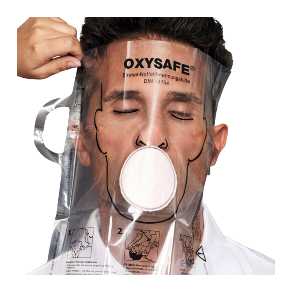 A person is wearing a transparent Holthaus Oxysafe® emergency ventilation aid mask from Holthaus Medical GmbH & Co. KG and has their eyes closed while another person adjusts the mask. The product is equipped with instructions and diagrams printed on the plastic surface.