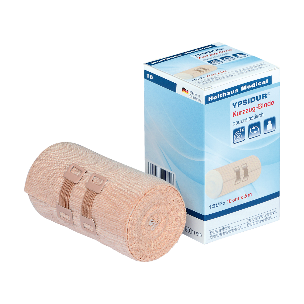 Ypsidur® short-stretch bandage with bandage clips from Holthaus Medical GmbH & Co. KG. The image shows a rolled-up permanently elastic short-stretch bandage next to its box. The beige bandage is fastened with two beige bandage clips, and the text on the box is predominantly in German and contains product details.