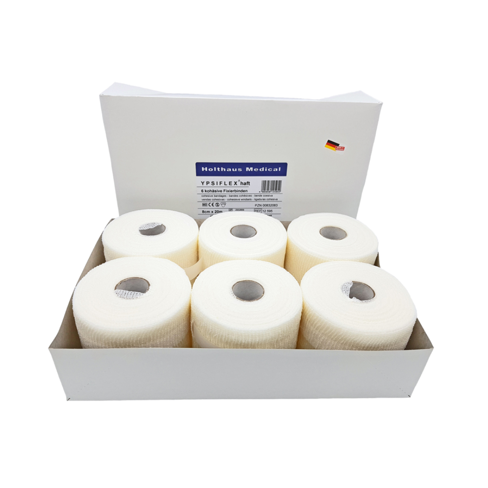 A box with six rolls of white medical adhesive tape labeled "Holthaus Ypsiflex® adhesive elastic gauze bandage, 20 meters" shows a small German flag symbol alongside other text. Each roll of Holthaus Ypsiflex® tape has a hole in the center, similar to elastic gauze bandage.