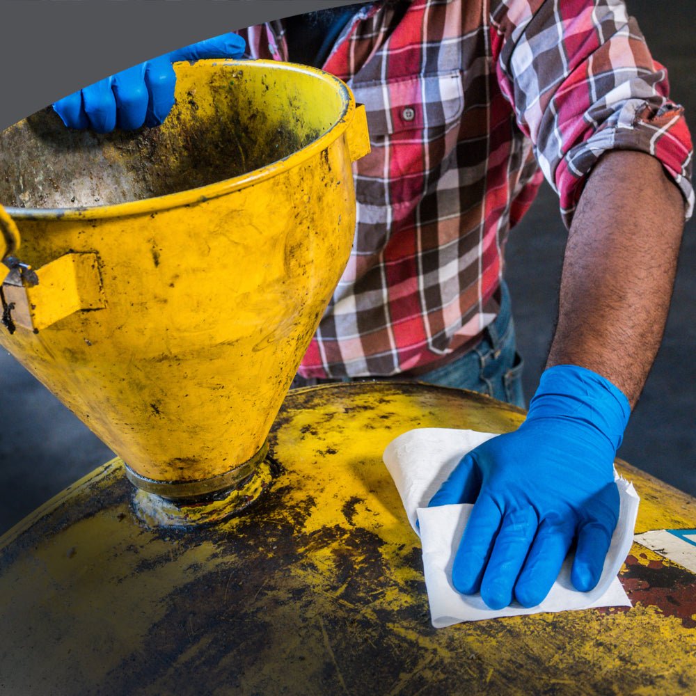 A person wipes the lid of a large yellow industrial container with a WypAll® X70 PowerClean large roll from Kimberly-Clark GmbH, demonstrating professional cleaning. A yellow funnel is attached to the container.