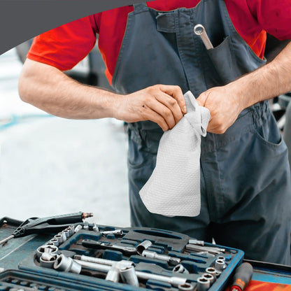 A person in a red shirt and gray coveralls wipes their hands with a white WypAll® X70 PowerClean towel from Kimberly-Clark GmbH next to an open toolbox with wrenches and screwdrivers.
