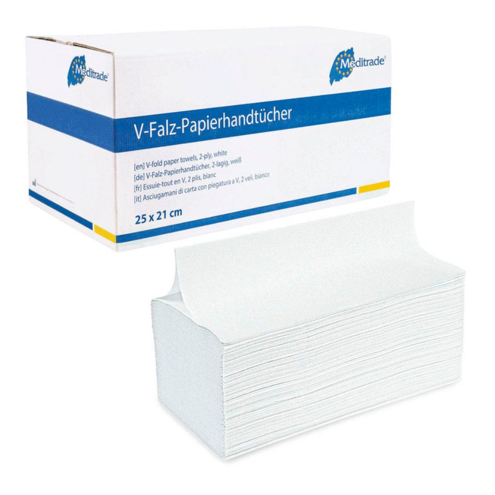 The image shows a box of folded paper towels with the label "Meditrade Folded Towels V-Fold 25x21cm 2-ply, white". The predominantly white box with blue accents contains high-quality paper towels in sizes 25 x 21 cm and with a two-ply construction. In front of the box is a stack of these folded towels from Meditrade GmbH, which are perfect for hand hygiene.
